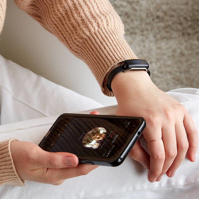 The black bracelet on a wrist with a phone in the other hand, showing how you connect the bracelet