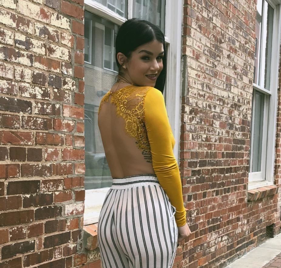 Reviewer wearing the long-sleeved bodysuit in yellow with lace on the top of the back and the rest cut out