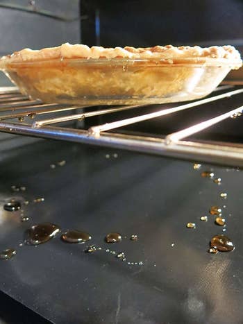 a pie cooking in the oven, dripping down onto the mat in the oven