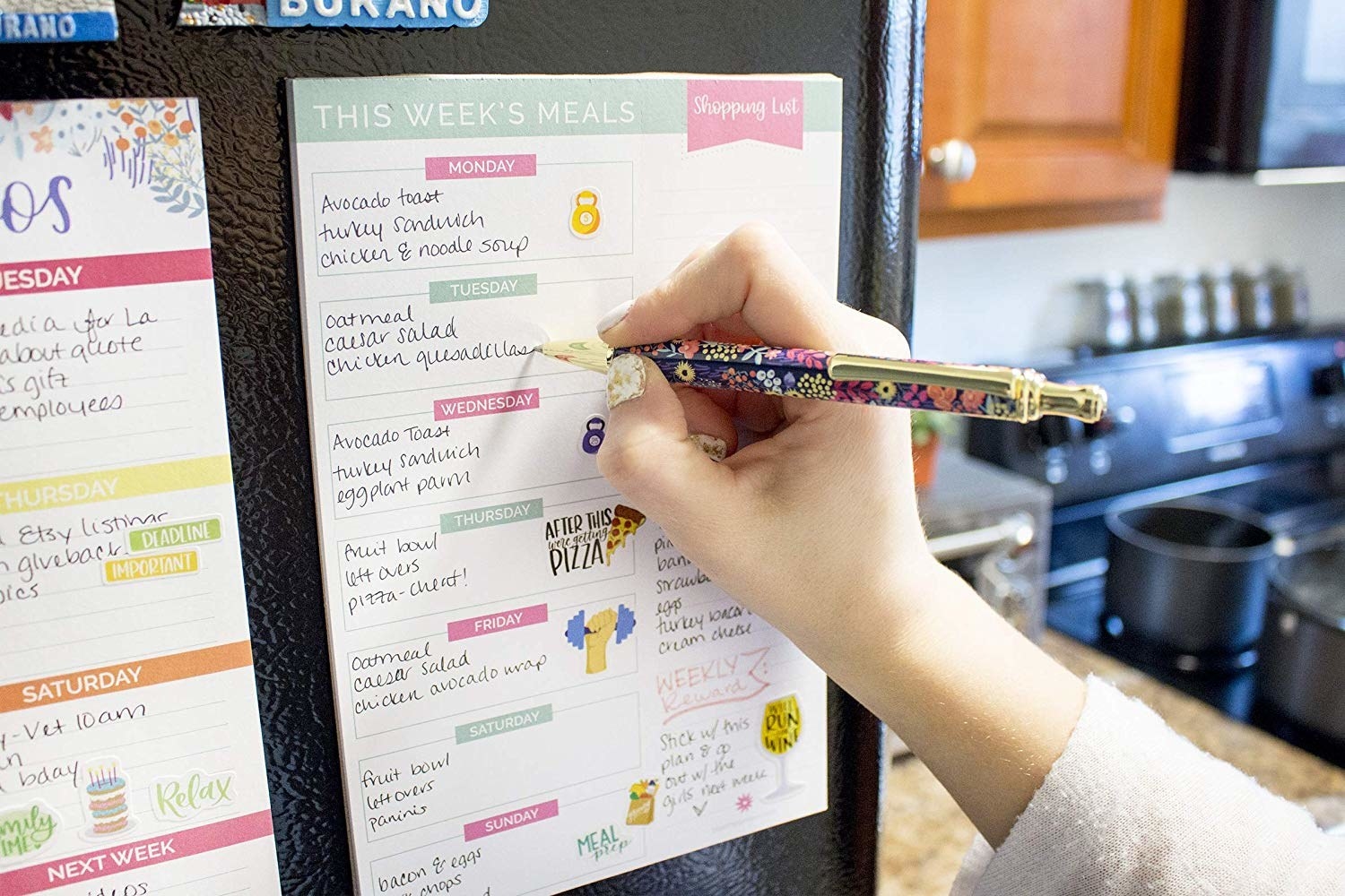 A model writing on the pad, which is on the refrigerator. The pad has spaces for every day of the week and a column for a shopping list