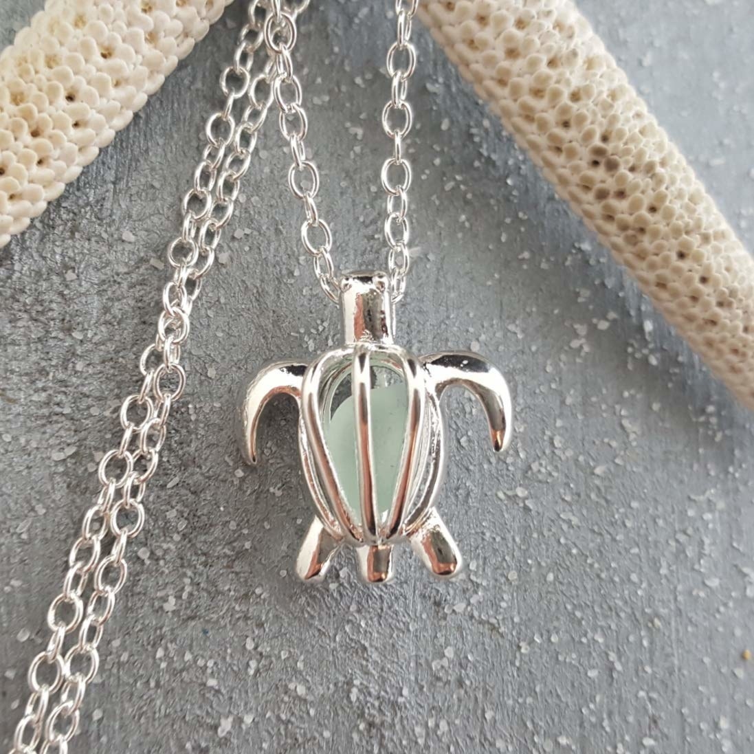 A silver hollow turtle-shaped necklace with a light green gem inside