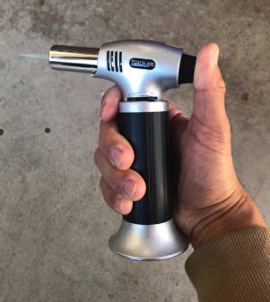 a hand holding the lit blow torch
