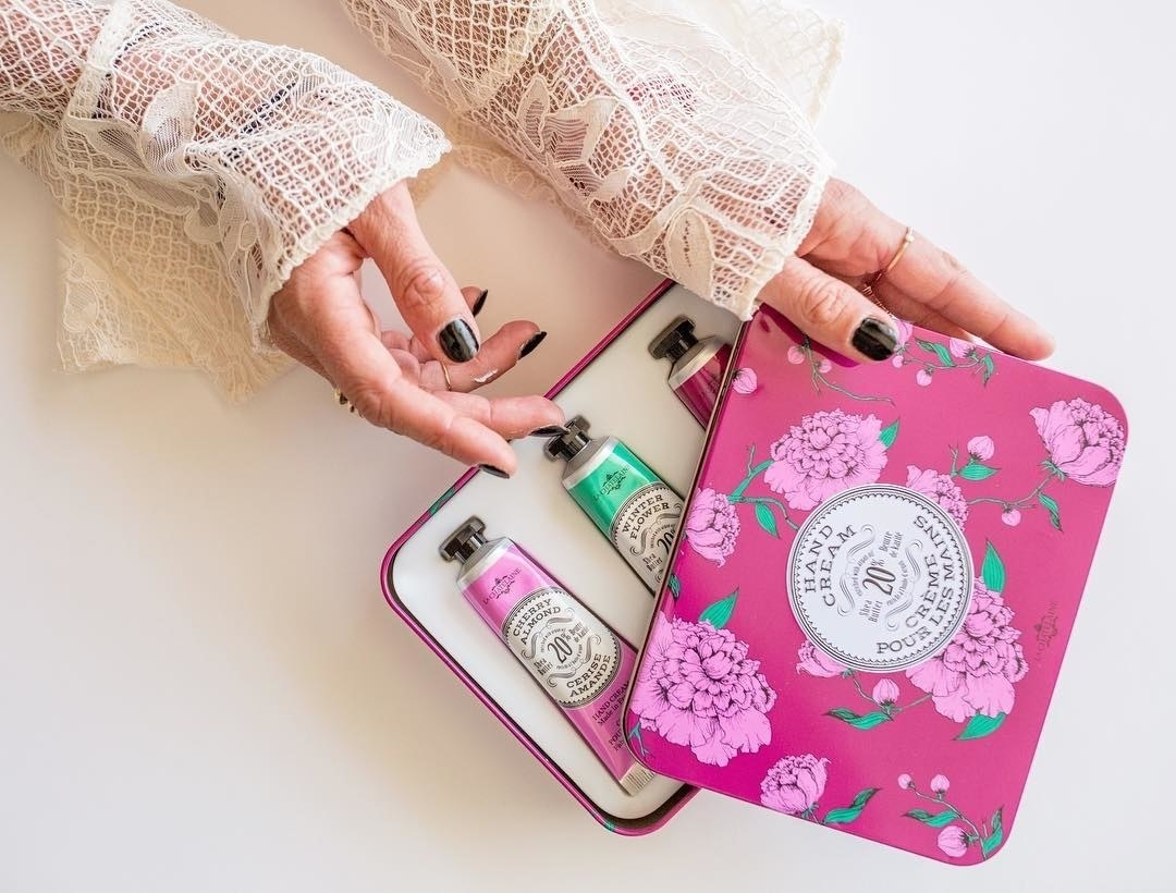 a model opening the pink tin and showing 3 hand creams inside