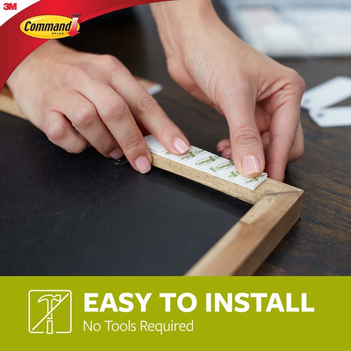A person installing the command strip on the back of a wooden frame.