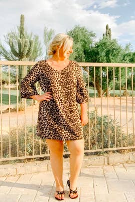 reviewer in leopard print bell sleeve dress wearing sandals and standing outside