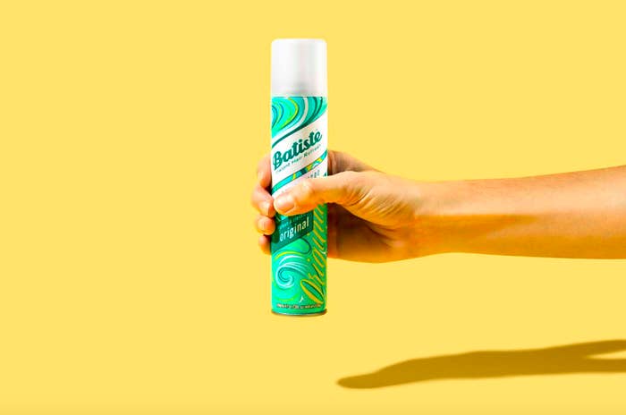 A hand holding a can of dry shampoo