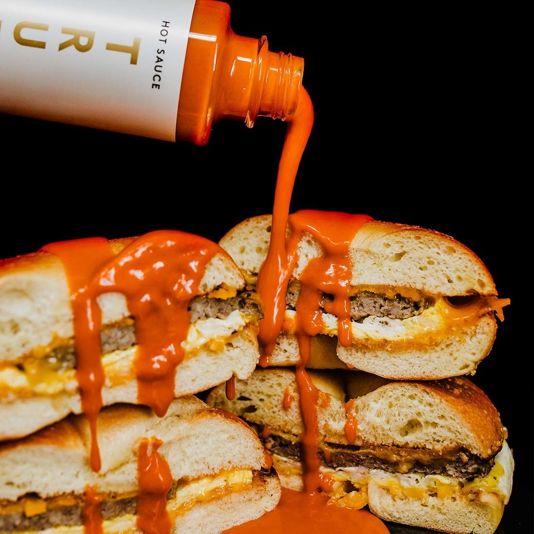 the hot sauce being poured on a stack of sandwiches