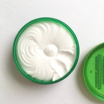 a green jar with a spiral patterned cream inside. a reviewer took a bit out with their fingers to show the consistency 