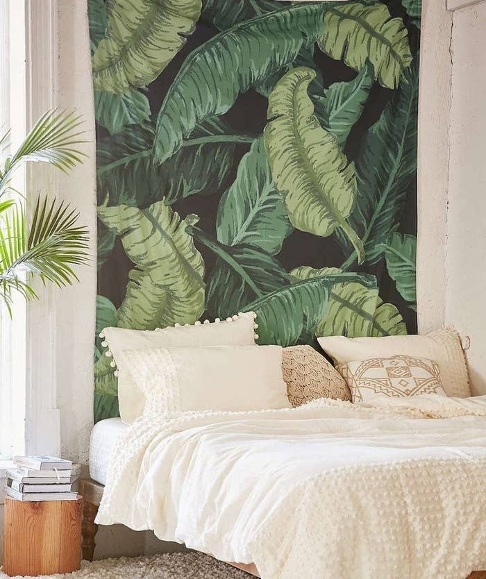 A bed in front of the banana leaf tapestry on a bedroom wall