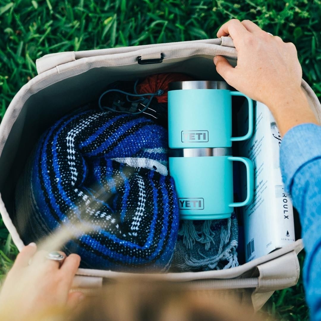 A person opening a bag with a blanket and two YETI mugs inside