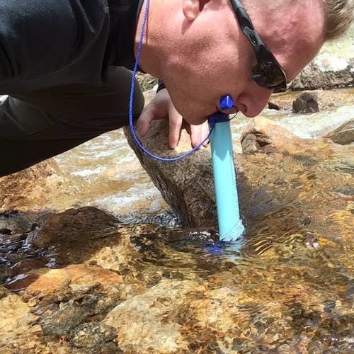 reviewer drinking from a stream with the lifestraw