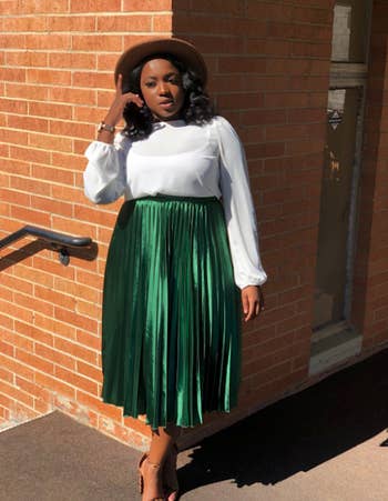 reviewer wearing the satin dark green skirt with a white long sleeve top and hat