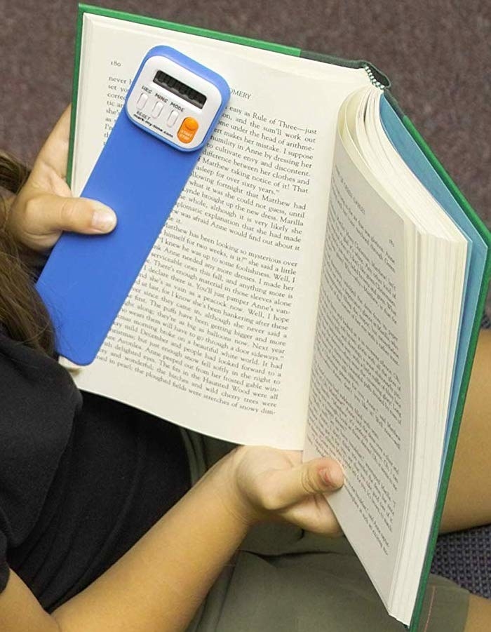 a kid holding their book and the bookmark which has buttons on it and a digital face that keeps up with the time