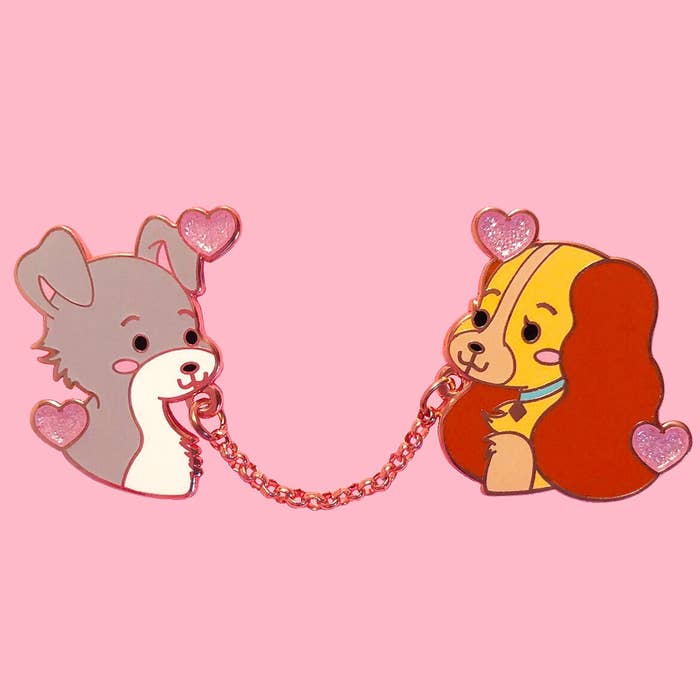 two pins of the lady and tramp connected with a chain that&#x27;s meant to look like spaghetti 