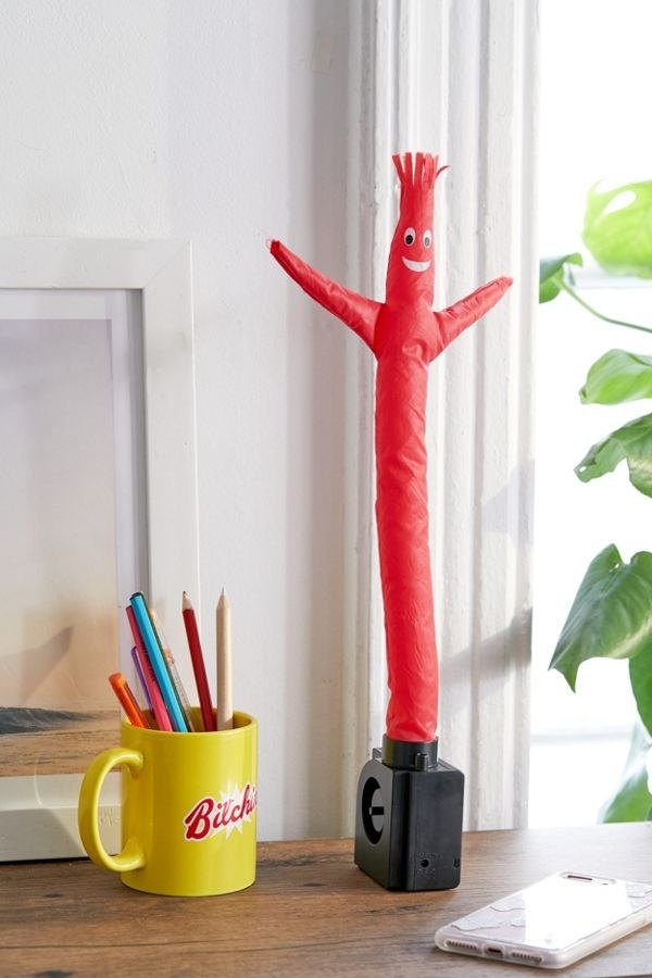 A small red air dancer towers over a mug on a desk