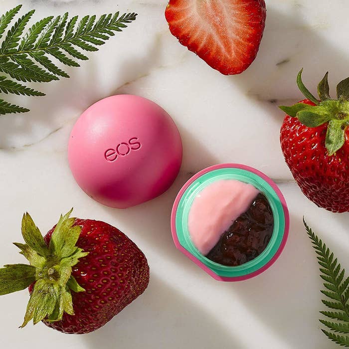 A small round container of lip balm with fresh strawberries around it