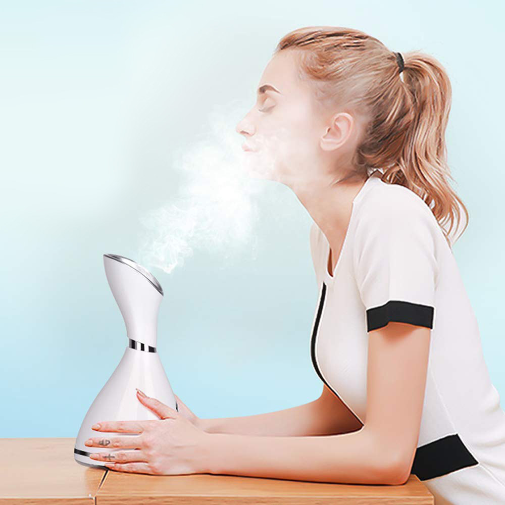 A person leaning toward a small steaming machine on the table in front of them