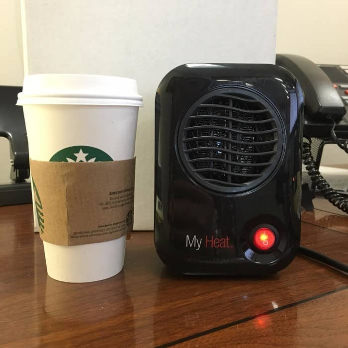 A reviewer showing their small black heater, about the same height as a starbucks coffee cup