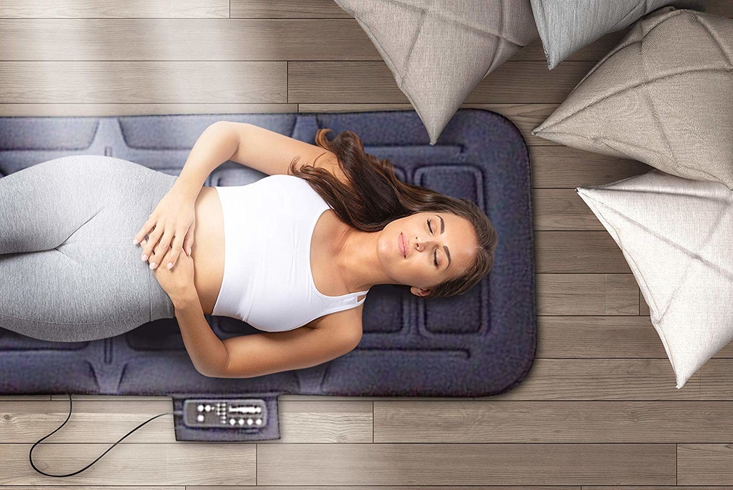 Person laying on padded massage mat that&#x27;s slightly larger than a yoga mat. It has a connected remote. 