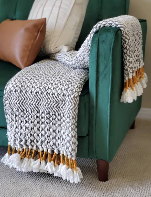 A customer review photo of the woven blanket in grey and white with mustard yellow accents