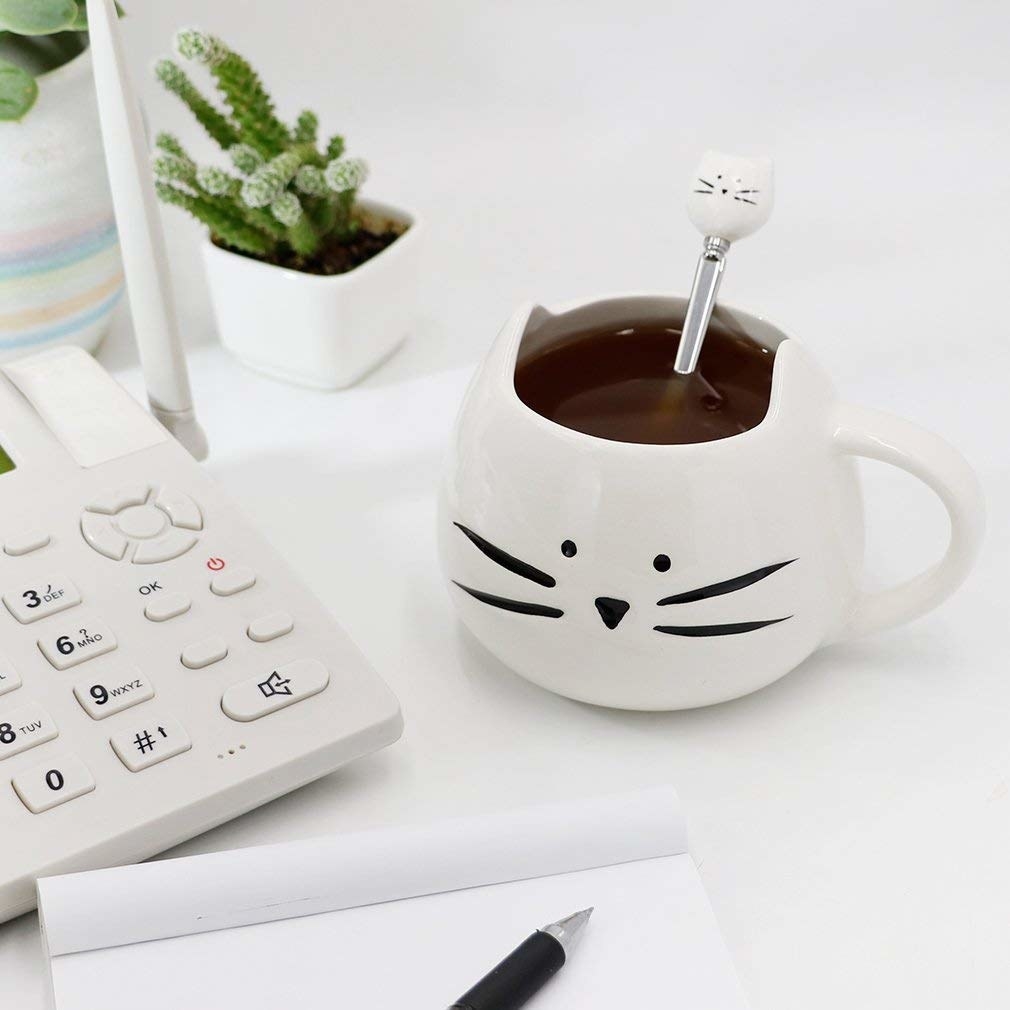 A small mug with a cat face on it sitting on a desk