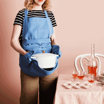 gif of a model wearing the blue apron and grabbing a pot with the built-in oven mitts on the sides to protect their hands