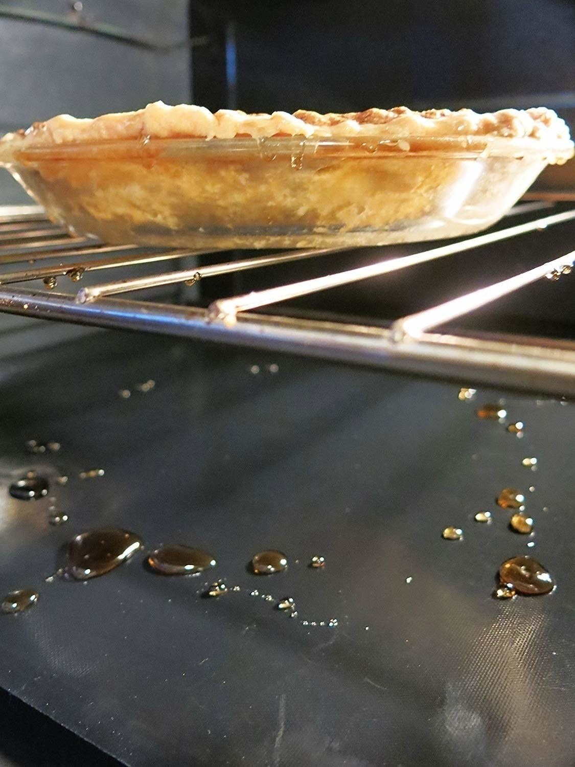 an apple pie inside the oven that has dripped liquid onto a mat below it