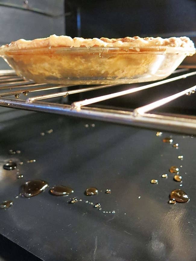 the oven liner covered in goo on the bottom of an oven, which has a pie baking in it