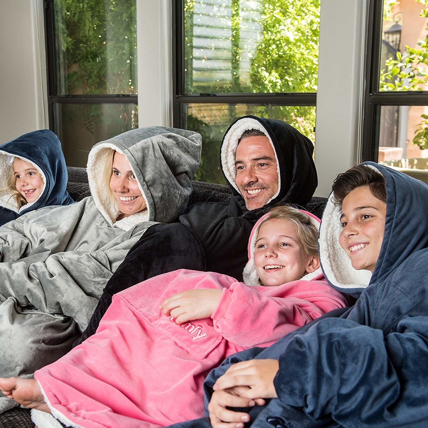family sitting on a couch, all wearing the, fleece-lined, oversized hoodies made from velvet-like blanket material 