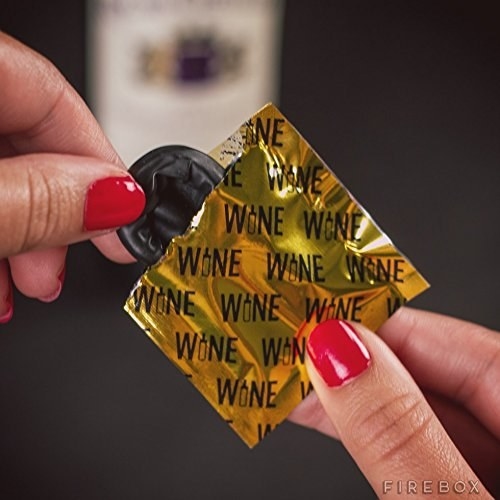 model&#x27;s hands pulling the black wine condom out of a gold wrapper