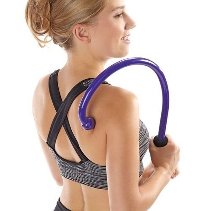 A model using the large hook-shaped massager to target their mid-back / shoulder