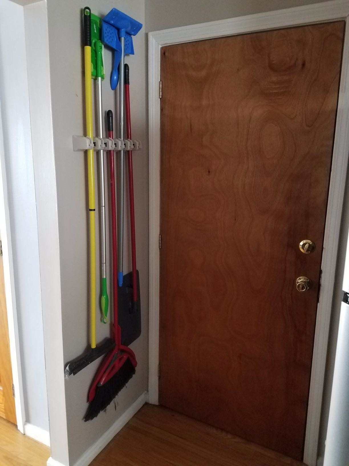 A reviewer with brooms and swiffers hanging from a small wall behind a door