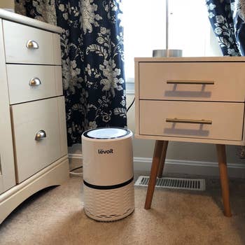 The air purifier in white sitting next to a nightstand