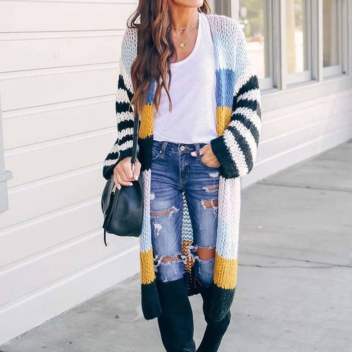 A person wearing a white top and ripped jeans. They are wearing the knitted cardigan as well.