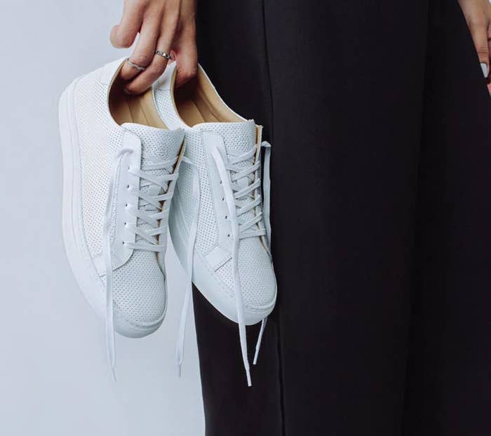hand holding the white sneakers with white soles and laces