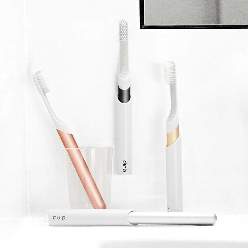 Four toothbrushes with white on top and rose gold, black, gold, and silver bottoms in their cases and a cup