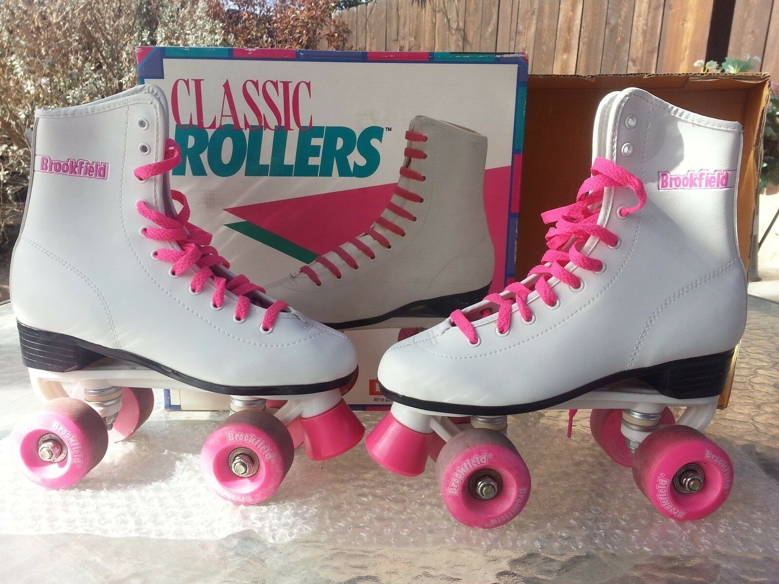 A pair of white roller skates with pink wheels and pink laces