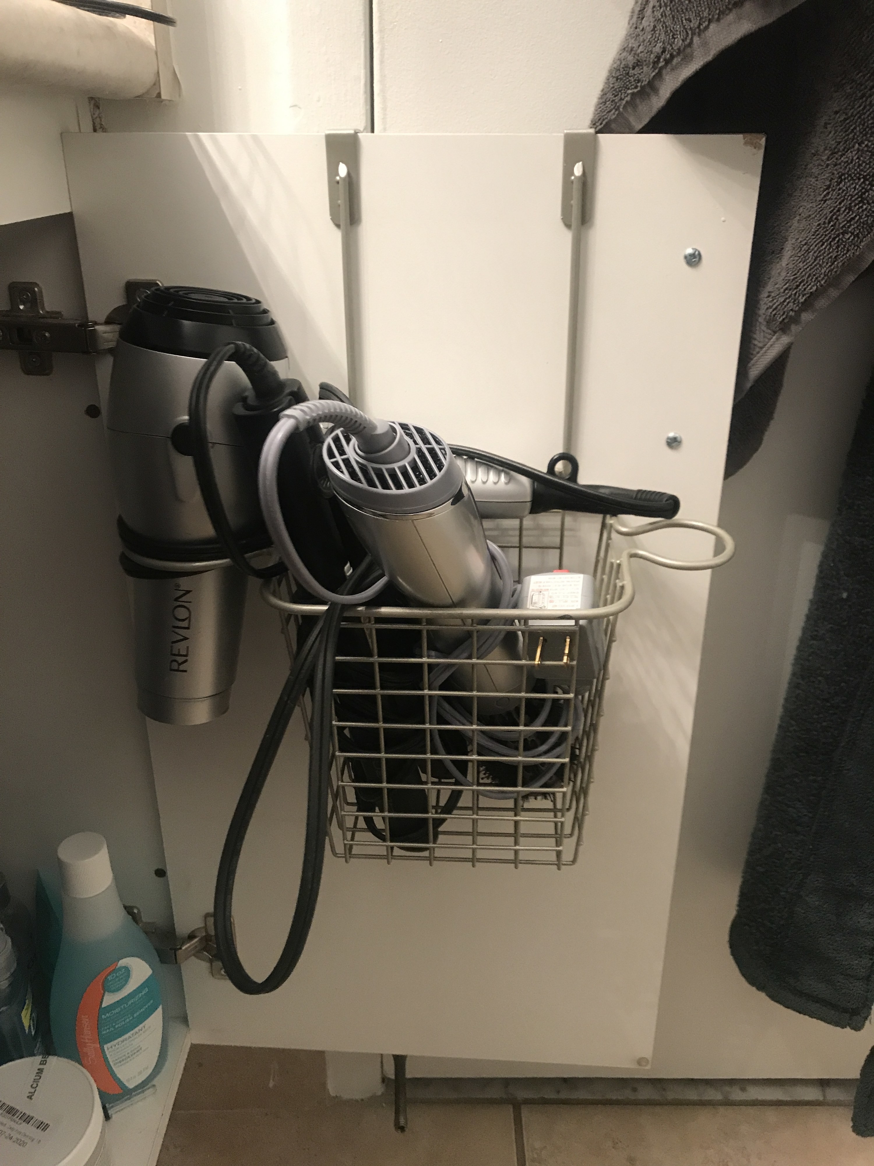 A small metal rack hanging on the inside of a bathroom cupboard and filled with hair styling tools