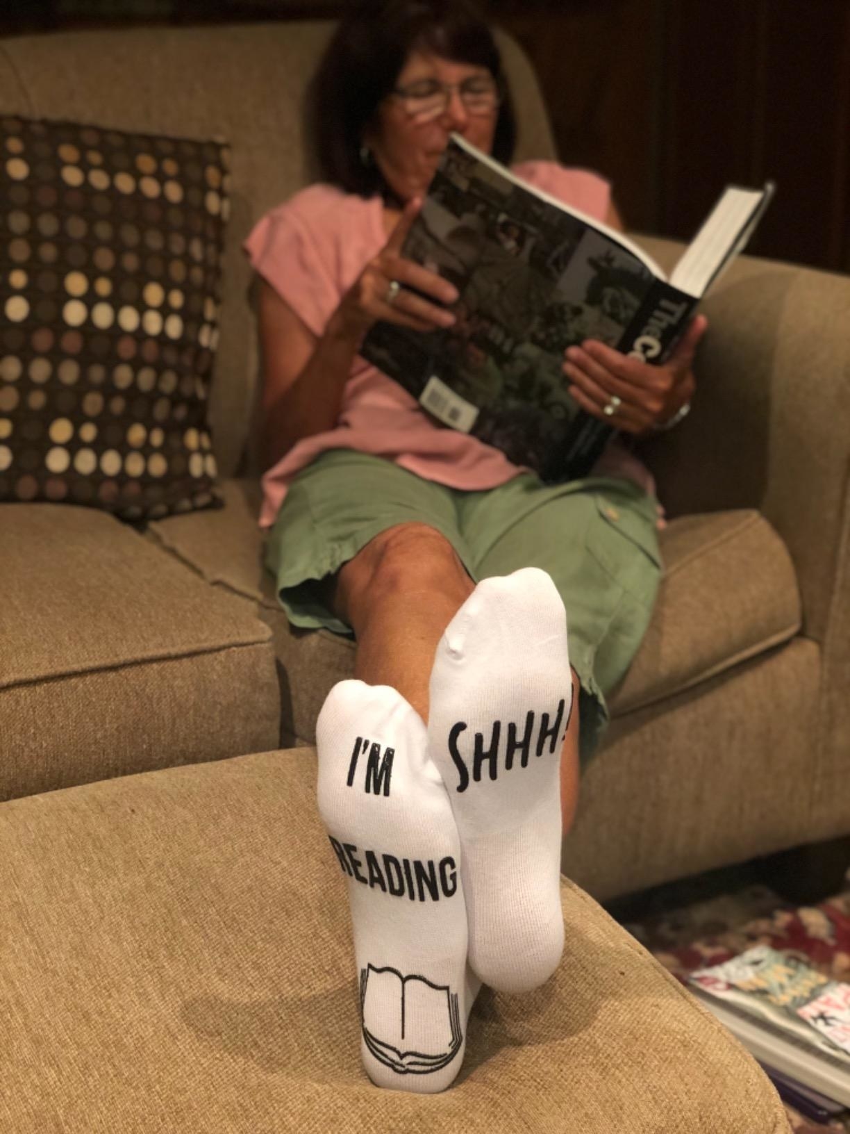 Reviewer photo of their mom wearing the socks which say, &quot;Shhh!&quot; and &quot;I&#x27;m reading&quot;