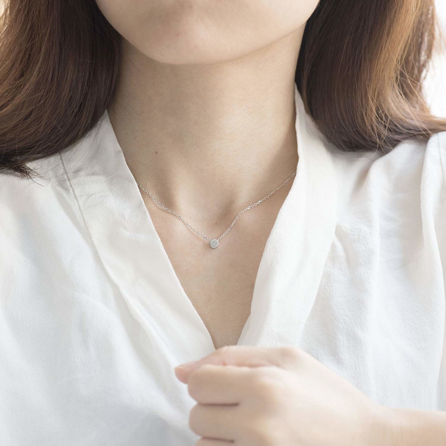 A model wearing a V-neck white shirt and a dainty silver dot necklace