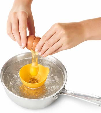 Hands cracking an egg in the poacher in a pot of water