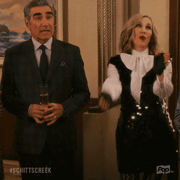 GIF of Johnny and Moira from Schitt&#x27;s Creek clapping and raising champagne glasses
