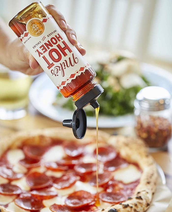 hand sqeezing a bottle of the hot honey on a pizza 