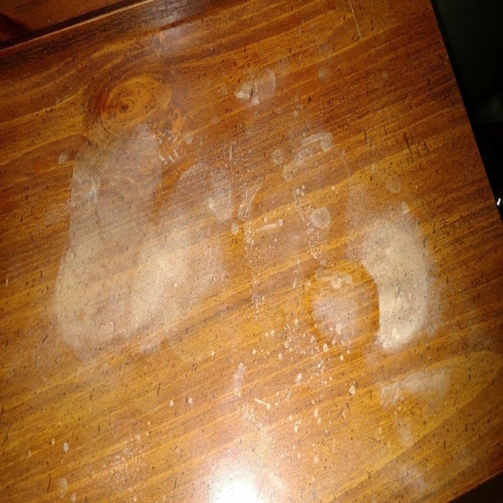 reviewer's photo of a wooden table with a lot of marks and stains on it 