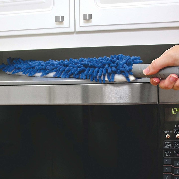 a hand using the duster to dust above a microwave 