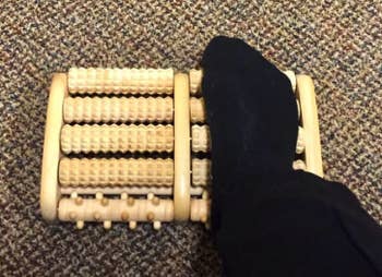a reviewer rolling their foot on the wooden massage roller
