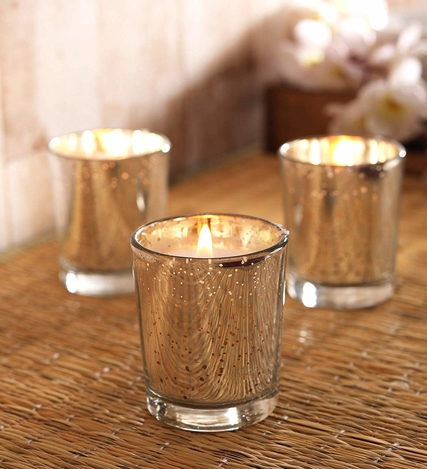 A set of three metallic glass holders on a table with lit candles inside them