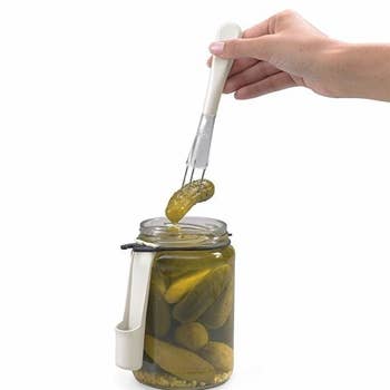 person grabbing a pickle with fork from jar