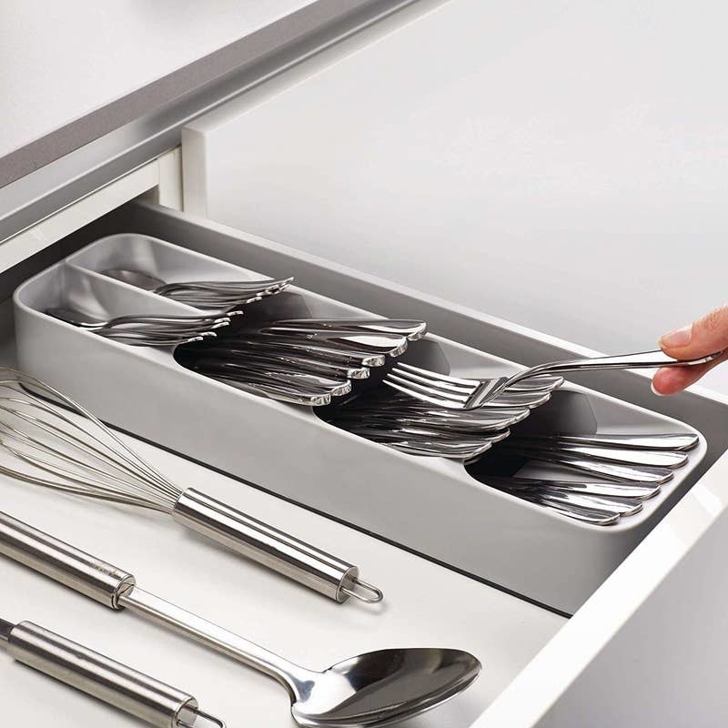Grey silverware tray with four slots filled with all different kinds of silverware in a drawer. 