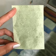 A hand holding one of the blotting sheets that visibly absorbed oil